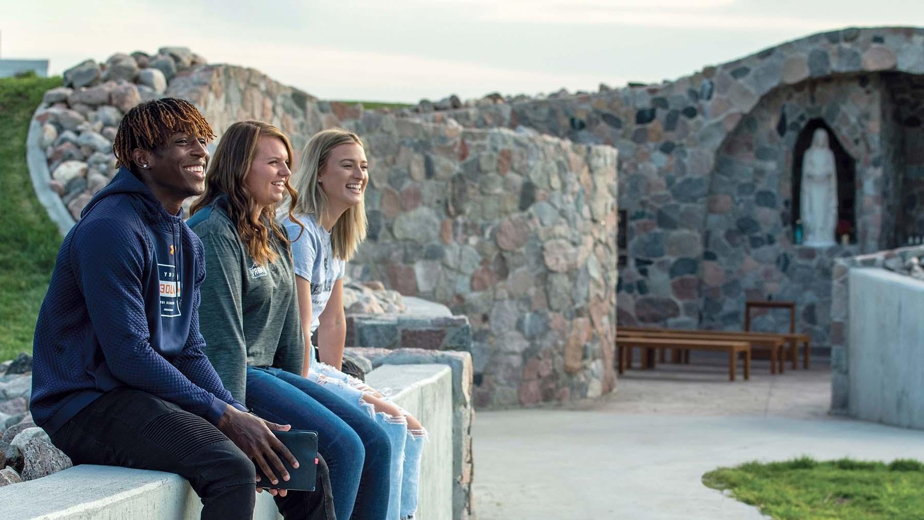 Smiling students sitting on wall outside of grotto